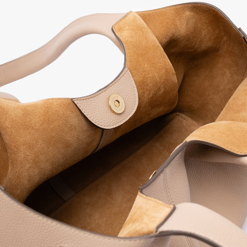 Close up of the suede interior lining and gold magnetic closure on STOW London's Hobo Tote in Camel pebbled leather on a light grey background