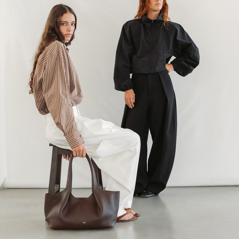 Models with STOW London's Hobo Tote in Black pebbled leather featuring a pleated front panel and gold-coated stainless steel hardware 
