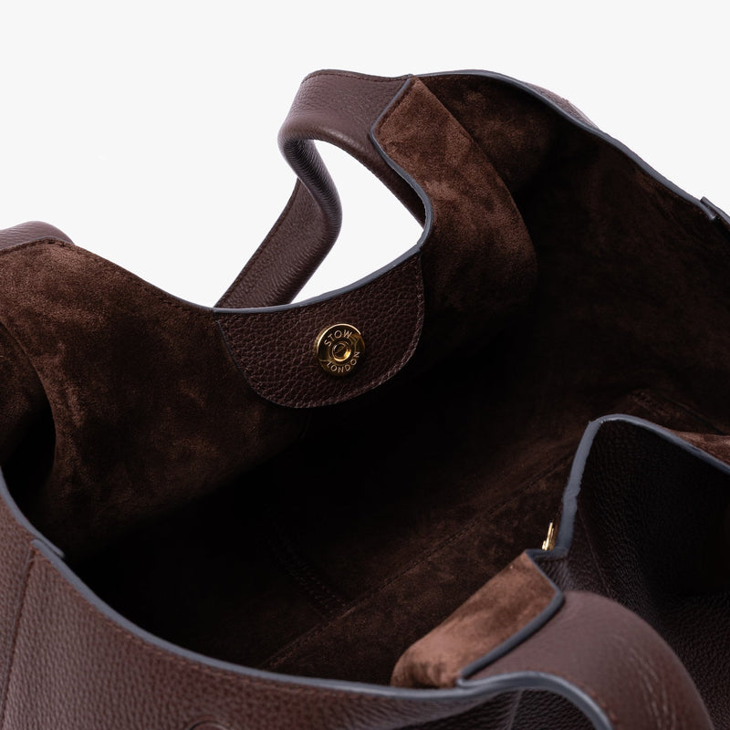 Close up of the Chocolate suede interior lining and gold magnetic closure on STOW London's Hobo Tote in Espresso pebbled leather on a light grey background 