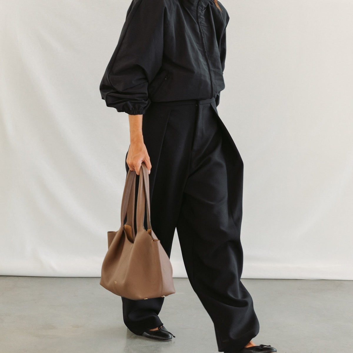 Model holding STOW London's Hobo Tote in Mocha pebbled leather featuring a pleated front panel and gold-coated stainless steel hardware 
