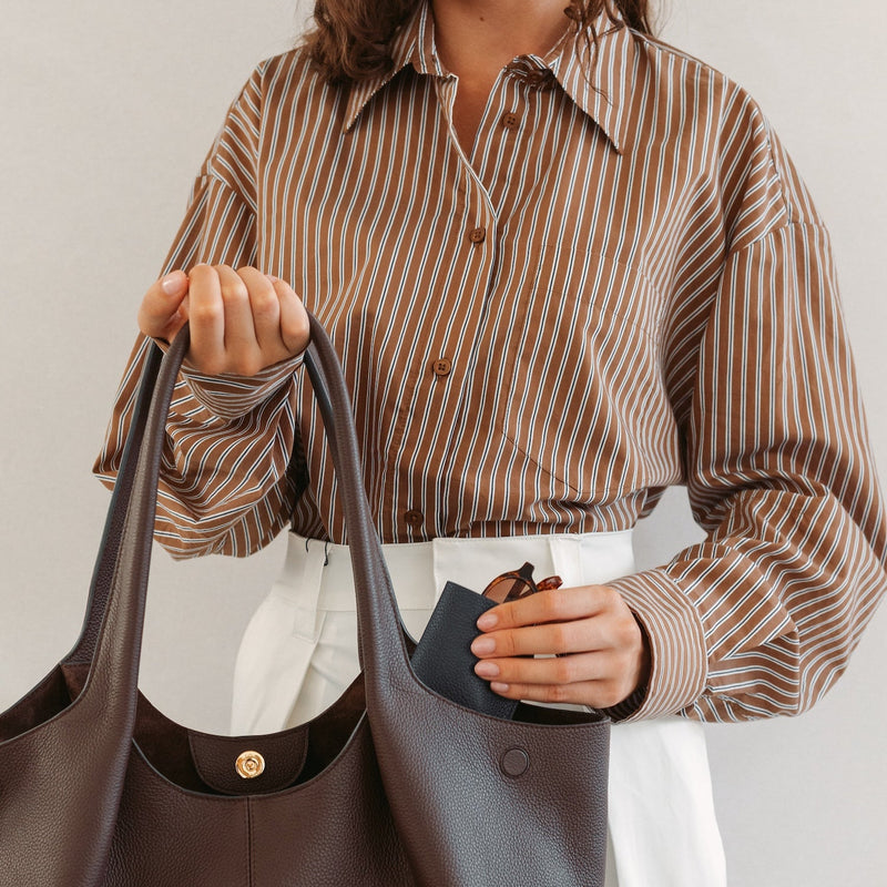 Model putting STOW London's Glasses Case in Navy pebbled leather into the Espresso Hobo Tote bag