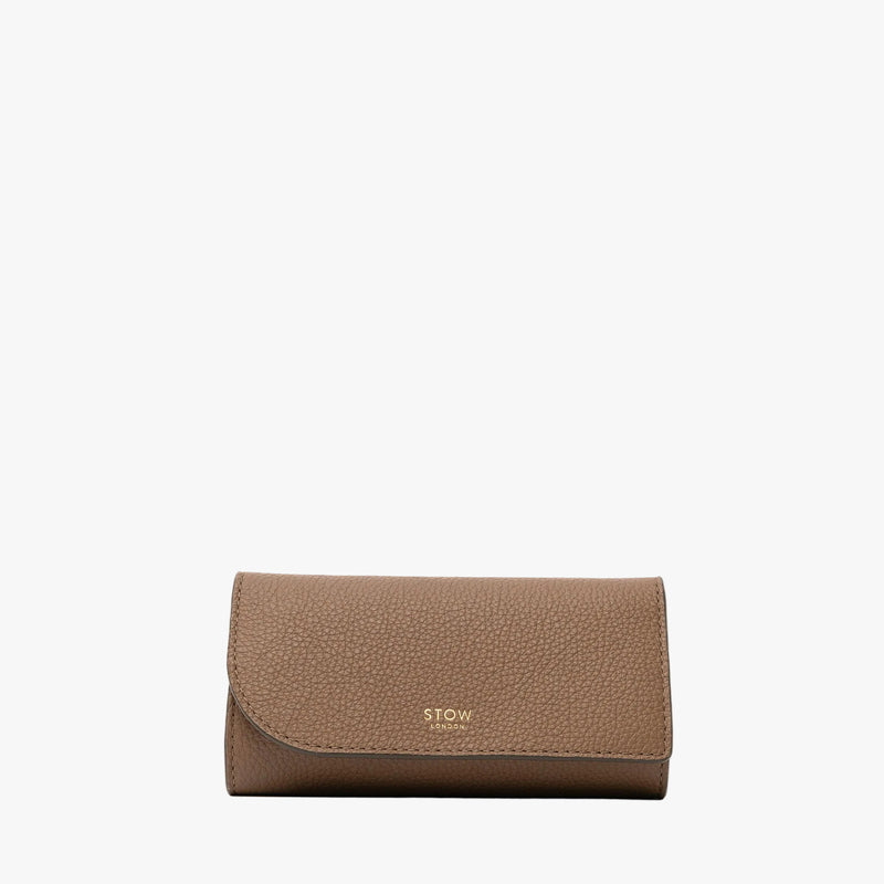 STOW London's Jewellery Roll in Mocha pebbled leather on a light grey background featuring a fine gold embossed logo on the front