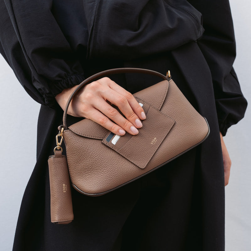 Model holding STOW London's Cardholder and Mini East West in Mocha pebbled leather featuring the matching lipstick case charm and a small gold embossed logo on the front