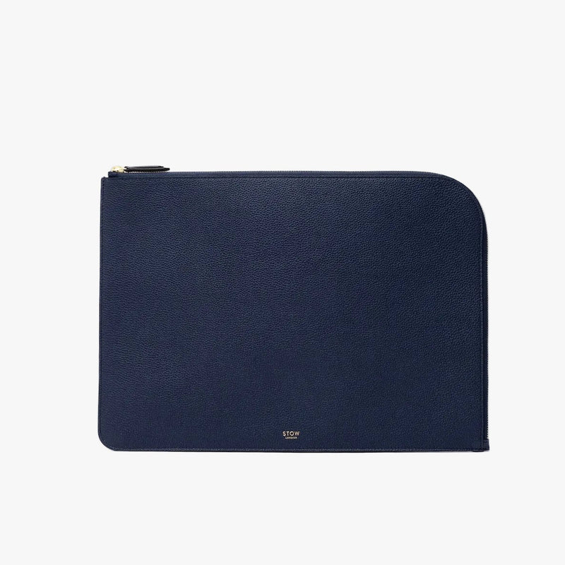 STOW London's Laptop Sleeve in Navy pebbled leather on a light grey background featuring a YKK Natulon Zip and a fine gold embossed logo on the front bottom. 