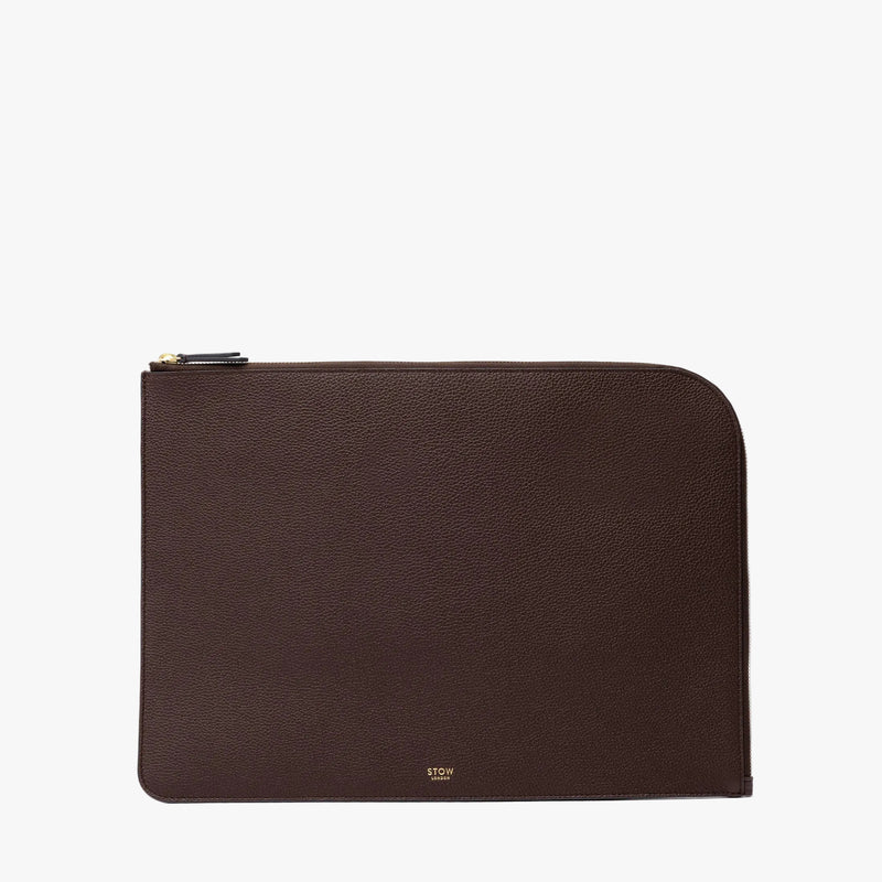 STOW London's Leather Sleeve in Espresso pebbled leather on a light grey background featuring a YKK Natulon Zip and a fine gold embossed logo on the front bottom. 