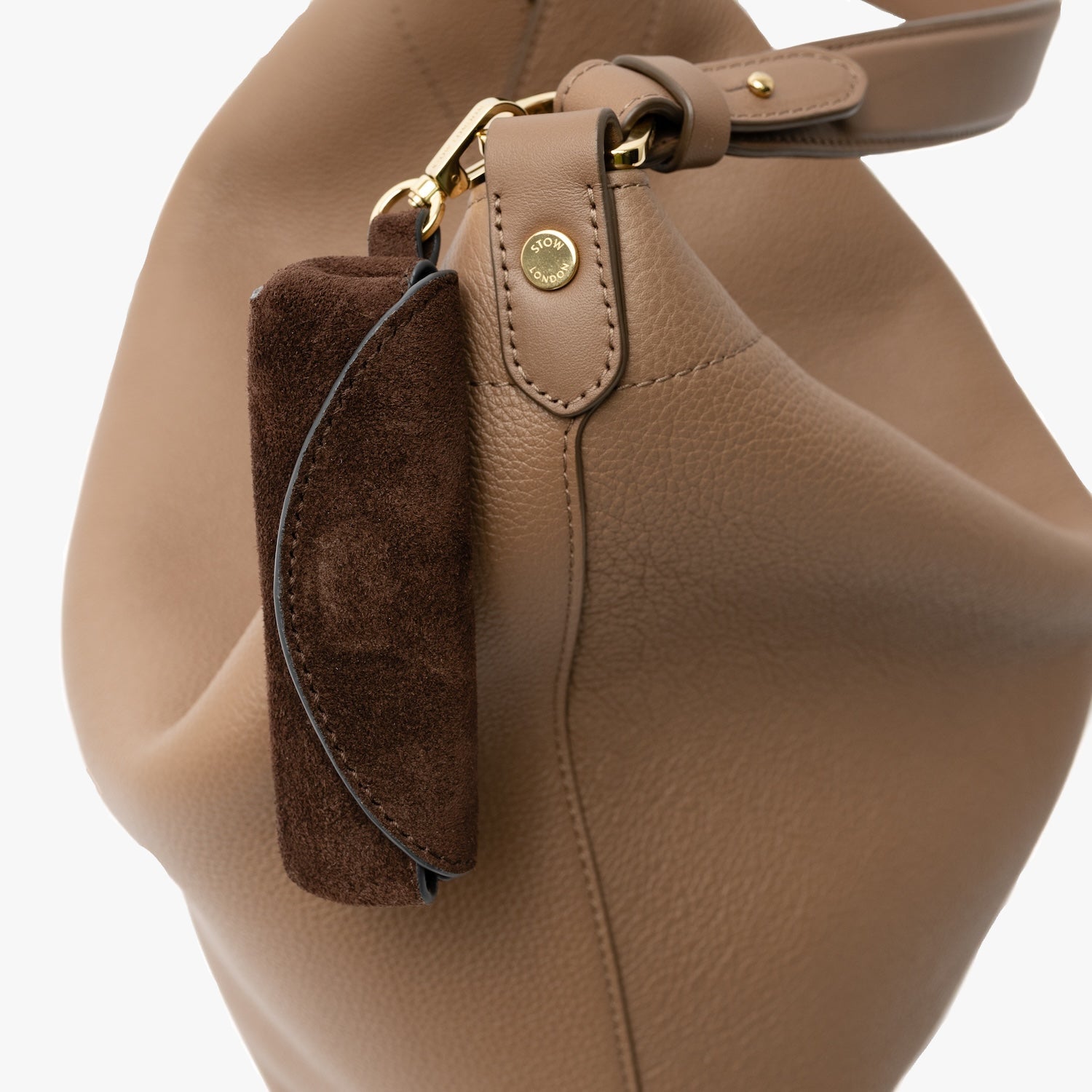 Close up of STOW London's Lipstick Case in Chocolate suede leather attached to the Mocha Maxi Curve bag on a light grey background featuring a gold-coated stainless steel clip