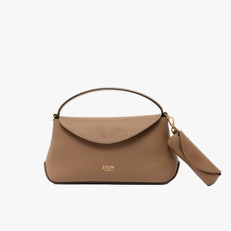 STOW London's Lipstick Case in Mocha pebbled leather on a light grey background attached to the matching Mini East West Bag by its gold-coated stainless steel clip