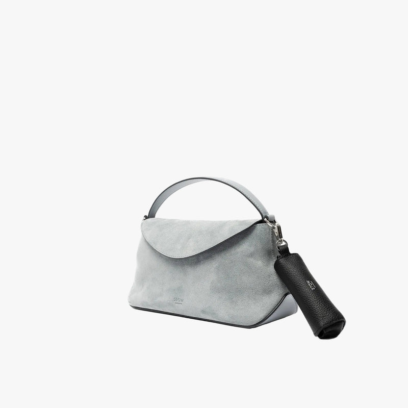 STOW London's Lipstick Case in Black pebbled leather attached by a silver stainless steel clip to the Misty Blue suede Mini East West on a light grey background