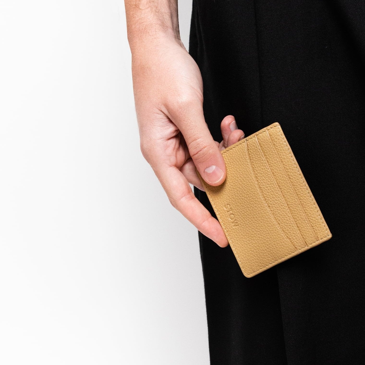 STOW London Leather Cardholder in Almond held by male model in studio wearing black trousers