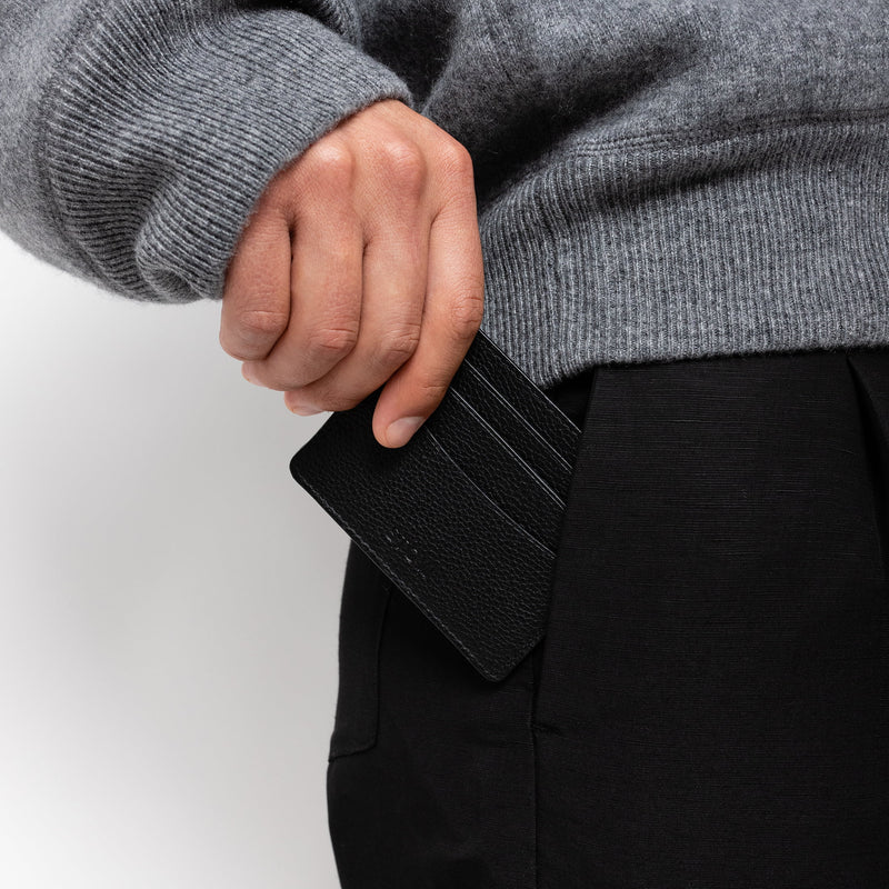 STOW London Cardholder in Black leather, studio image with male model placing cardholder into pocket
