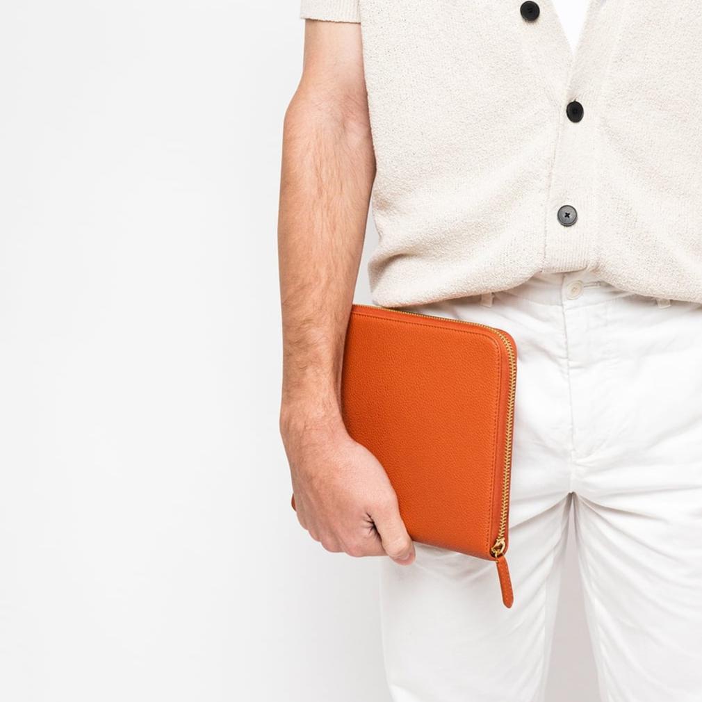 STOW London First Class Folio tech case in Clay Orange leather carried by male model in studio image