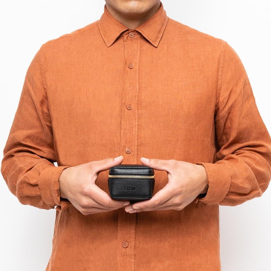 STOW London Hester Essentials Case in Black leather, held by model in studio image wearing rust coloured shirt