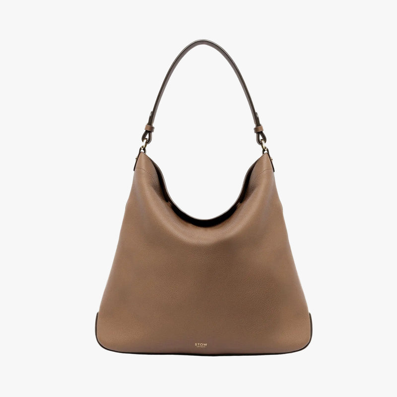 STOW London's Maxi Curve bag in Mocha pebbled leather featuring gold-coated stainless steel hardware on a light grey background