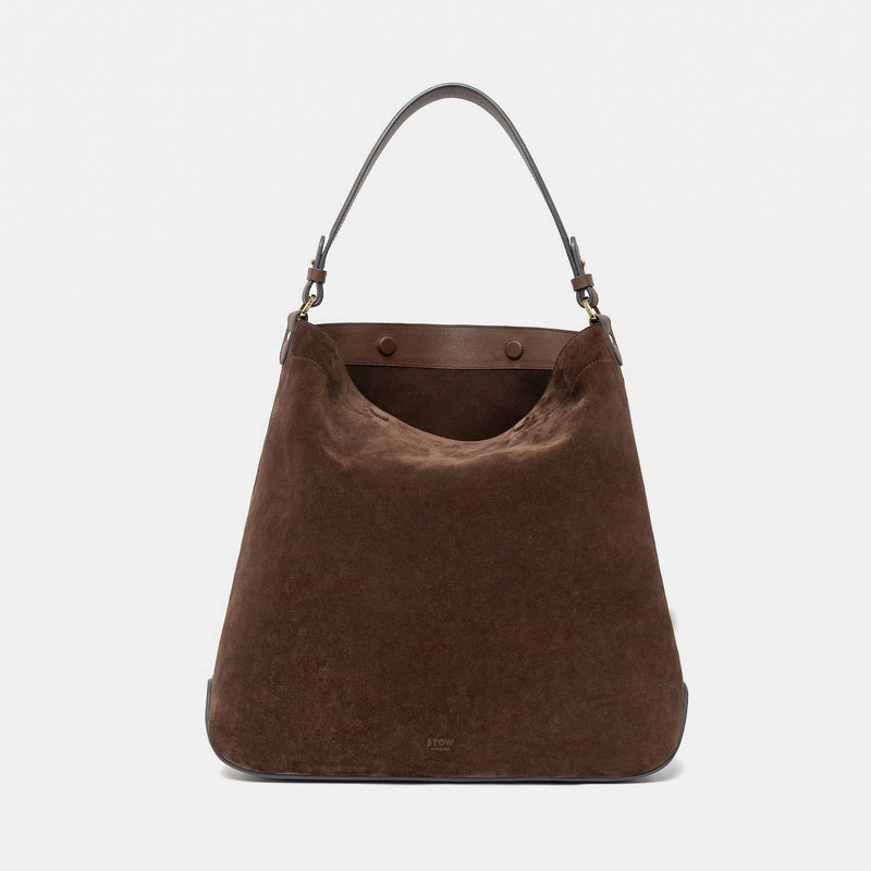 STOW London's Maxi Curve bag in Chocolate suede leather featuring gold-coated stainless steel hardware on a light grey background