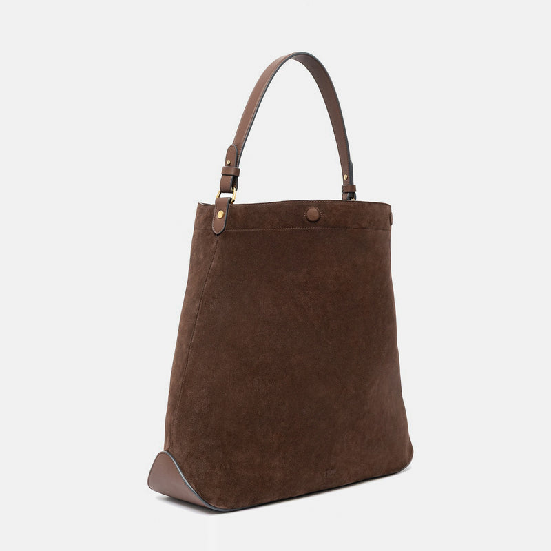 Off-axis view of STOW London's Maxi Curve bag in Chocolate suede leather with magnets open shaped as a bucket bag featuring gold-coated stainless steel hardware on a light grey background