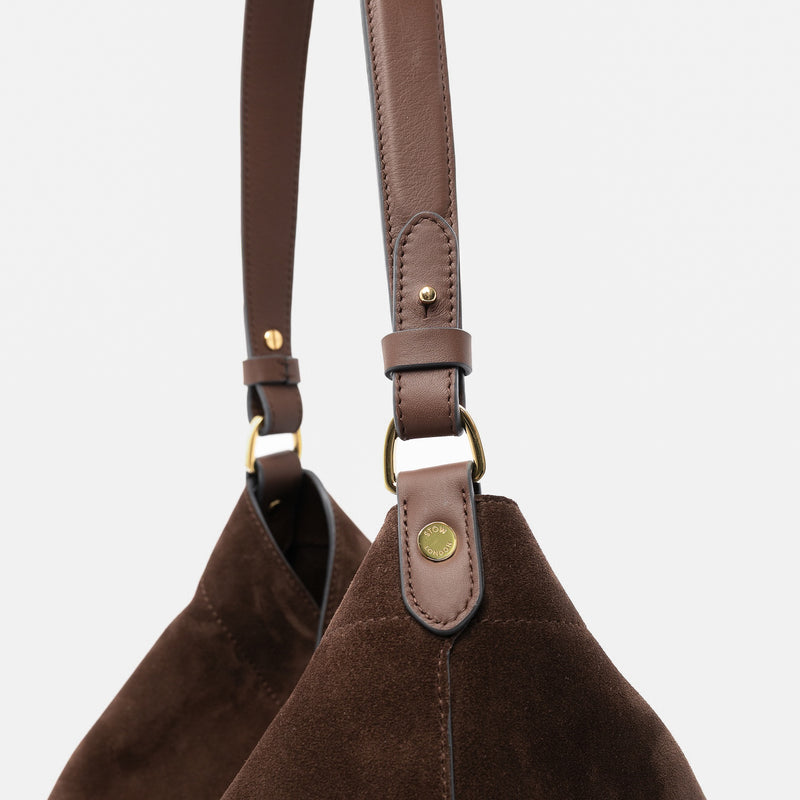 Close up of the handles on STOW London's Maxi Curve bag in Chocolate suede leather featuring gold-coated stainless steel hardware on a light grey background