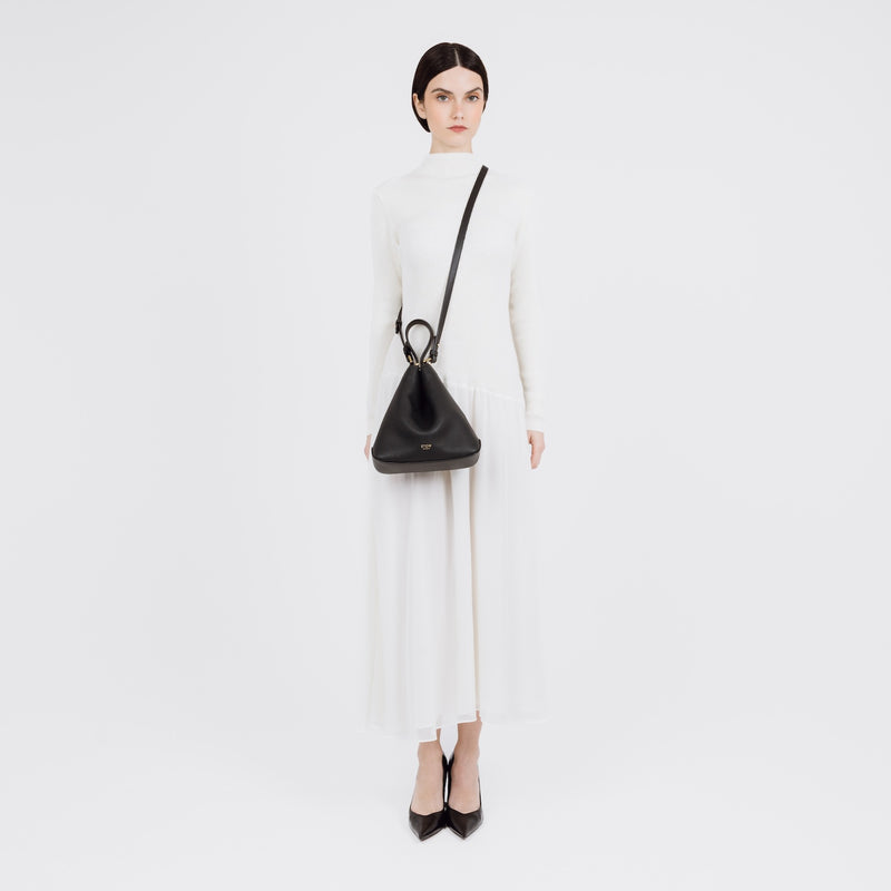 Model wearing STOW London's Midi Curve bag in Black pebbled and smooth leather crossbody in a triangular style featuring gold-coated stainless steel hardware on a white background