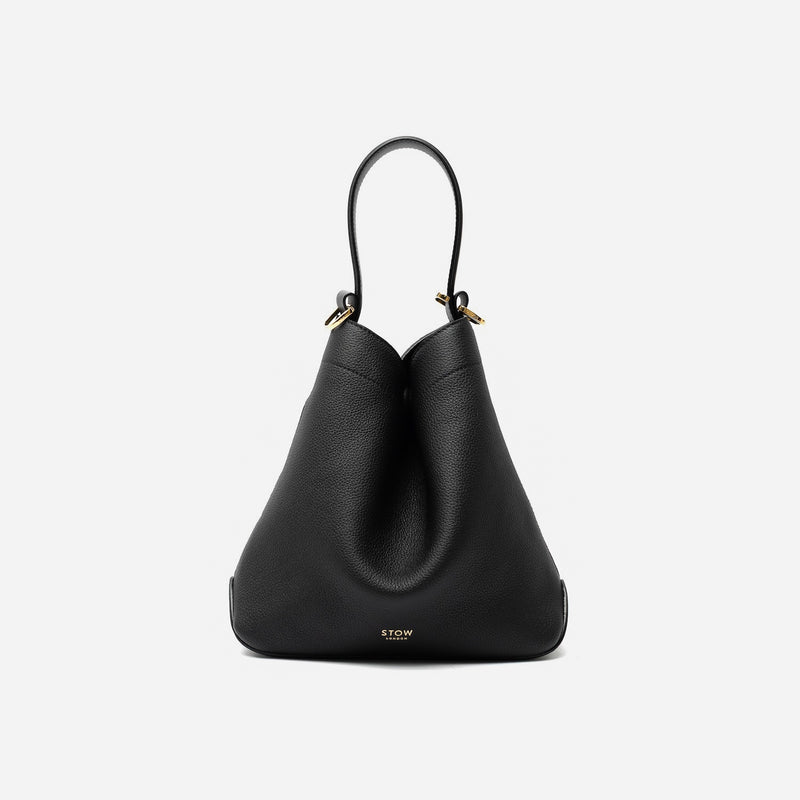 STOW London's Midi Curve in Black pebbled leather styled in a triangular shape featuring gold-coated stainless steel hardware on a light grey background