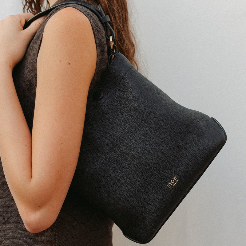 Model wearing STOW London's Midi Curve in Black leather featuring the detachable shoulder strap with gold hardware and details 