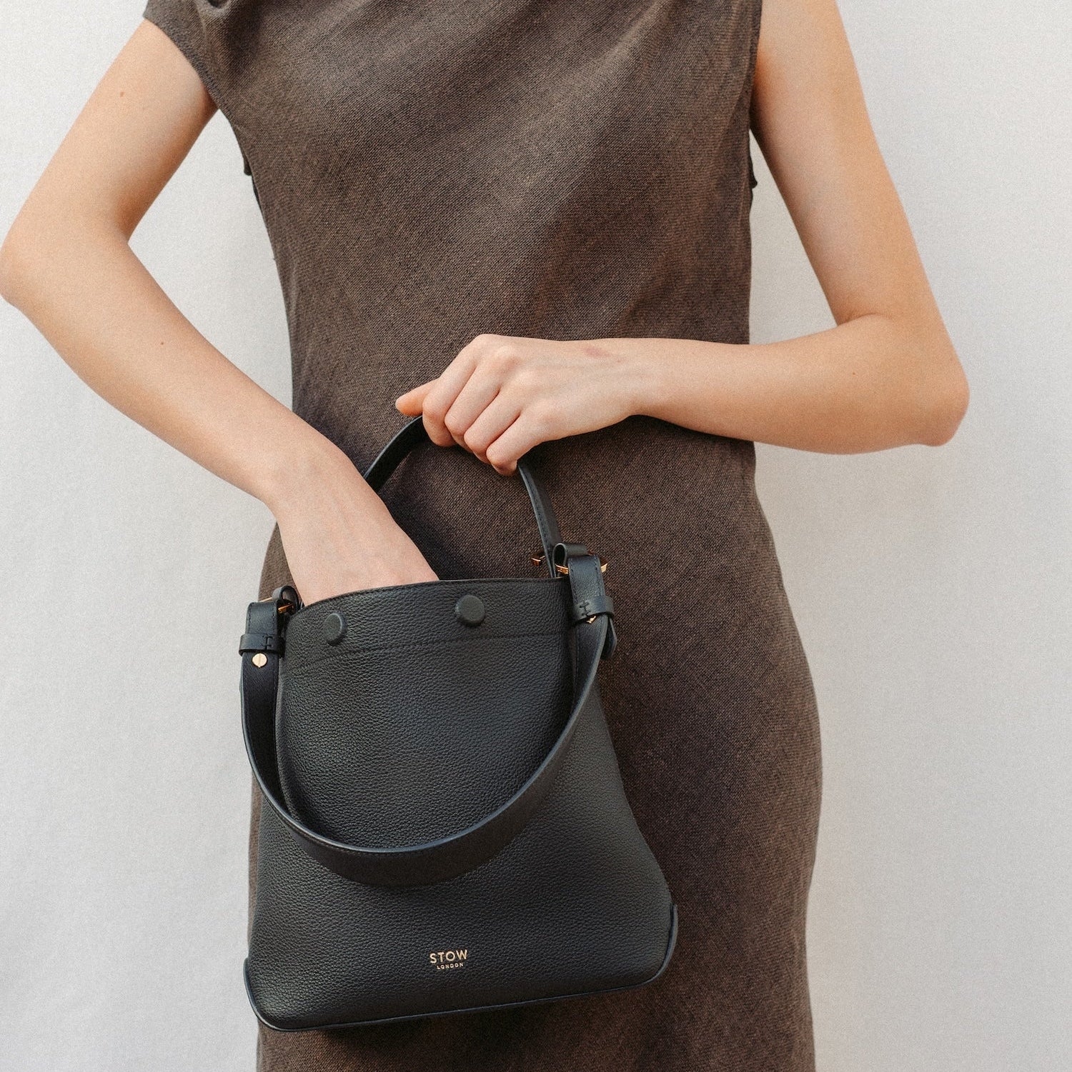 Model wearing STOW London's Midi Curve in Black leather featuring the detachable shoulder strap  and top handle with gold hardware and details 