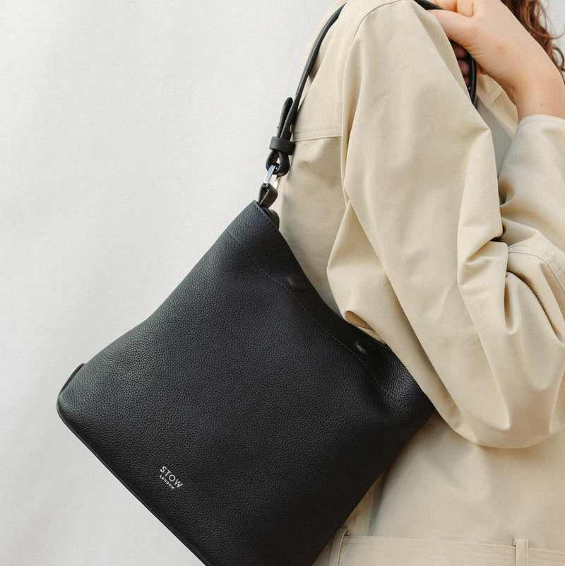 Model wearing STOW London's Midi Curve in Black leather featuring the detachable shoulder strap with silver hardware and details 