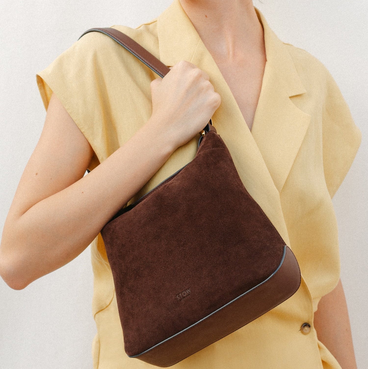 Model wearing STOW London's Midi Curve in Chocolate suede leather featuring the detachable shoulder strap with gold hardware 