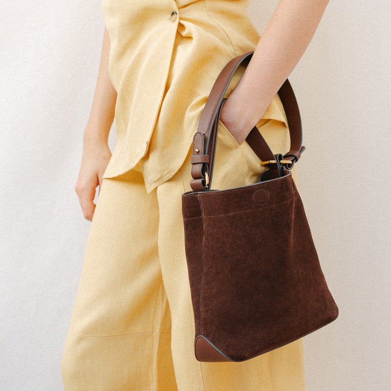 Model wearing STOW London's Midi Curve in Chocolate suede leather featuring the detachable shoulder strap with gold hardware 