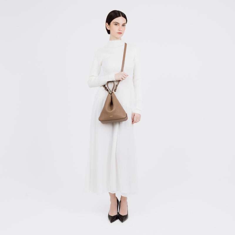Model wearing STOW London's Midi Curve bag in Mocha pebbled and smooth leather crossbody shaped in a soft triangular style featuring gold-coated stainless steel hardware on a white background