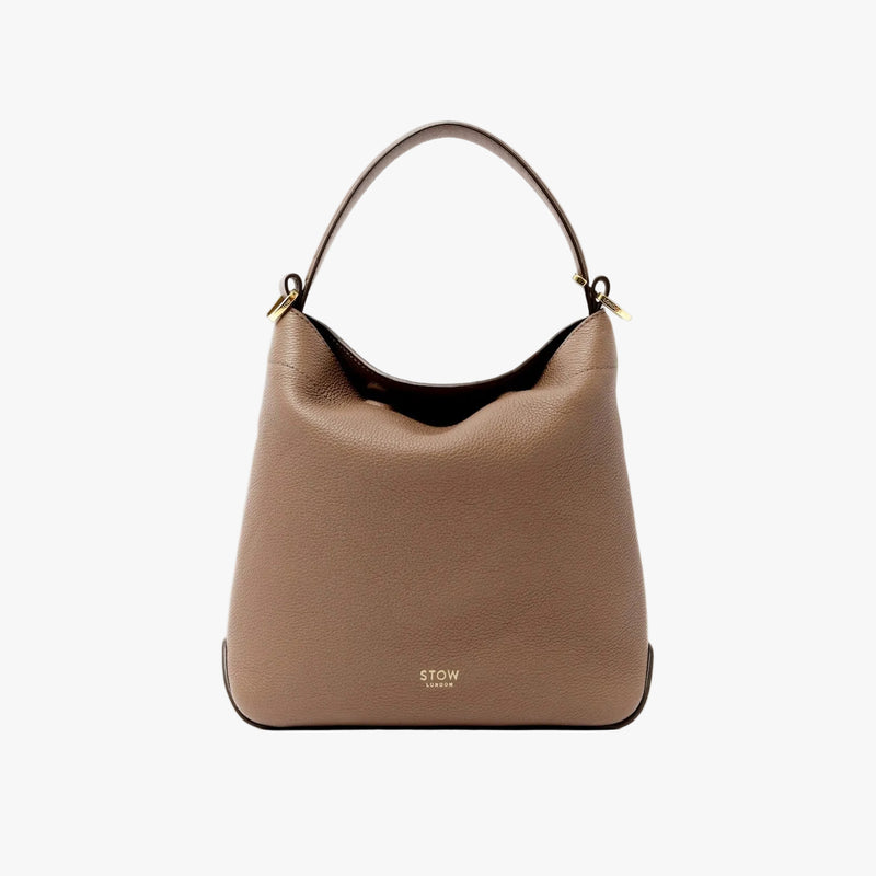STOW London's Midi Curve bag in Mocha pebbled leather styled as a flap bag featuring gold-coated stainless steel hardware on a light grey background