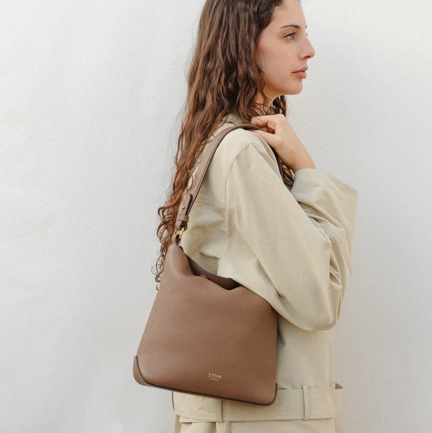 Model wearing STOW London's Midi Curve in Mocha leather featuring the detachable shoulder strap with gold hardware and details 