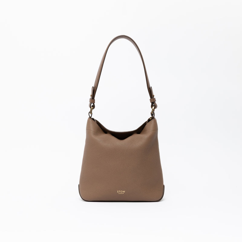 STOW London's Midi Curve and detachable shoulder strap in Mocha leather on a light grey background featuring gold hardware and details 
