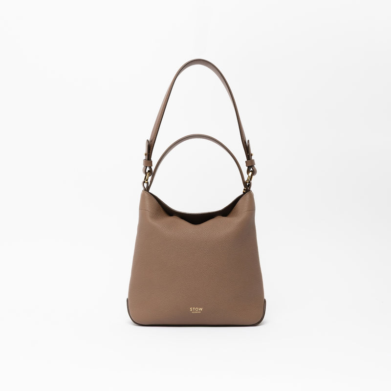STOW London's Midi Curve, detachable shoulder strap and top handle in Mocha leather on a light grey background featuring gold hardware and details 