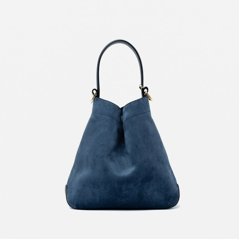 STOW London's Midi Curve in Navy suede leather styled in a triangular form featuring gold-coated stainless steel hardware on a light grey background