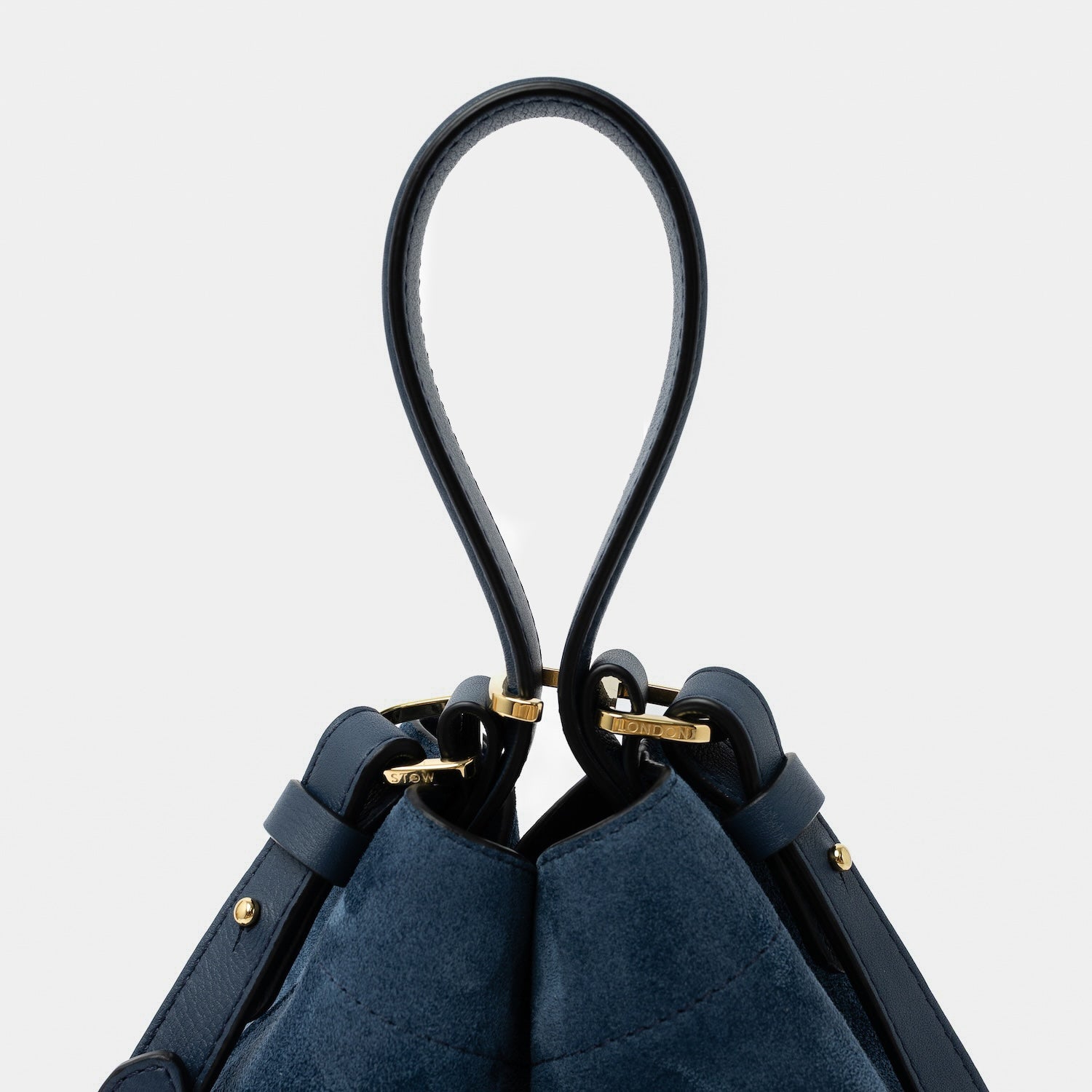 Close up of the handle on STOW London's Midi Curve in Navy suede leather featuring gold-coated stainless steel hardware, clip and detachable crossbody strap on a light grey background