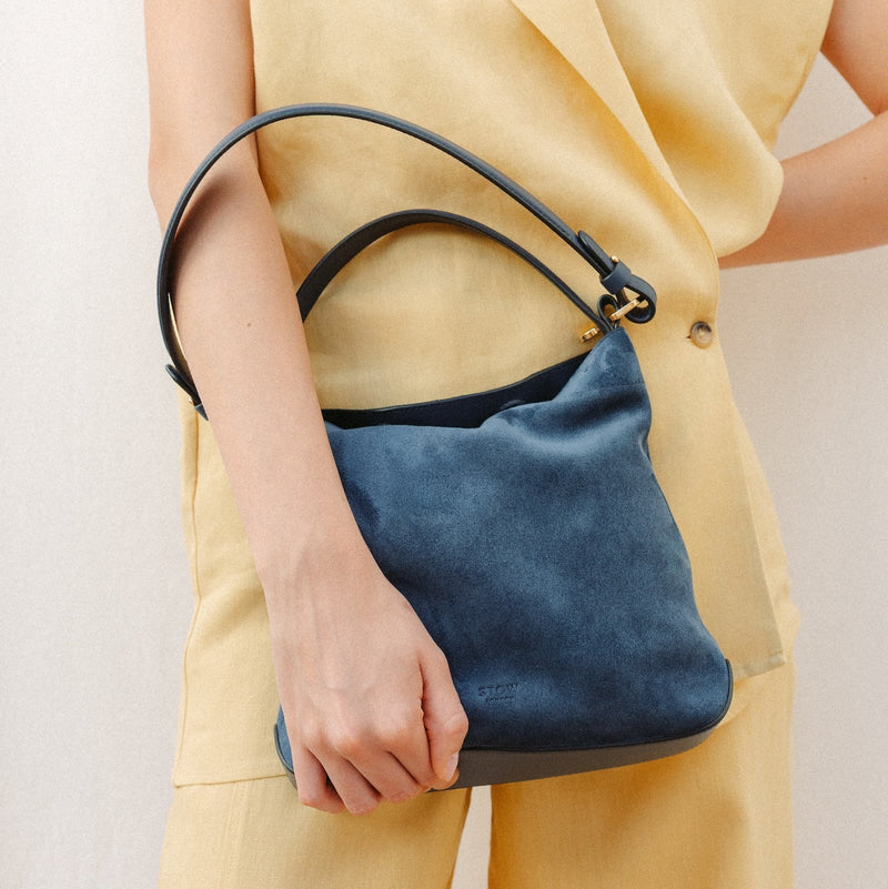 Model wearing STOW London's Midi Curve in Navy leather featuring the detachable shoulder strap with gold hardware