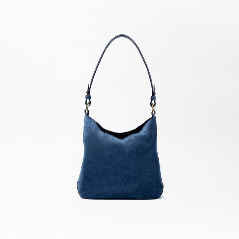 STOW London's Midi Curve in Navy suede leather on a light grey background featuring the detachable shoulder strap with gold hardware and details 