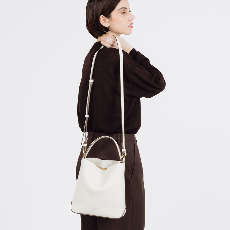 Model holding STOW London's Midi Curve bag in Spring Moon pebbled and smooth leather over her shoulder featuring gold-coated stainless steel hardware on a white background