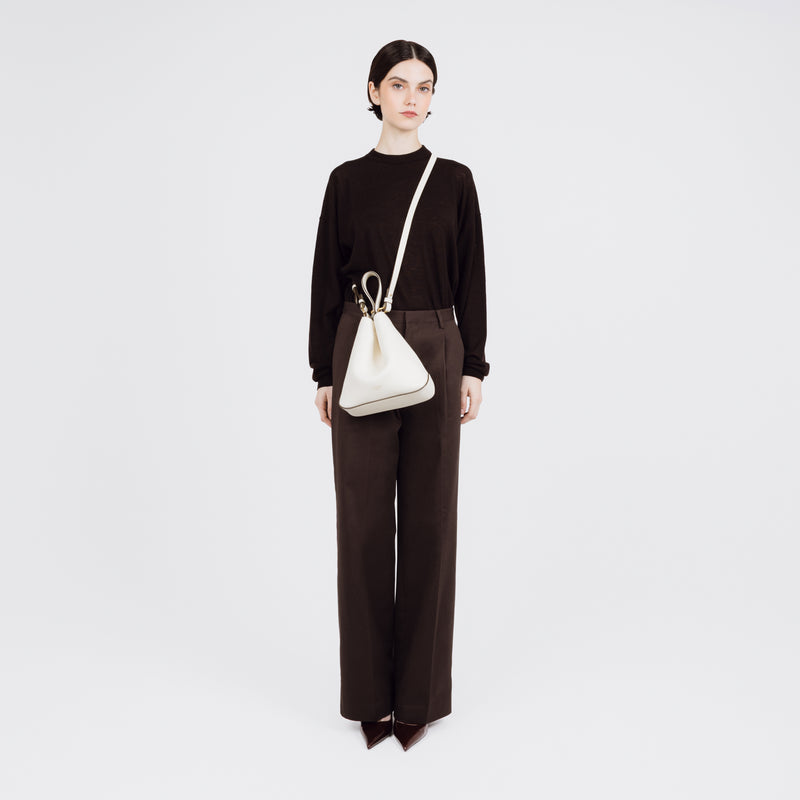 Model wearing STOW London's Midi Curve bag in Spring Moon pebbled and smooth leather crossbody styled in a triangular shape featuring gold-coated stainless steel hardware on a white background