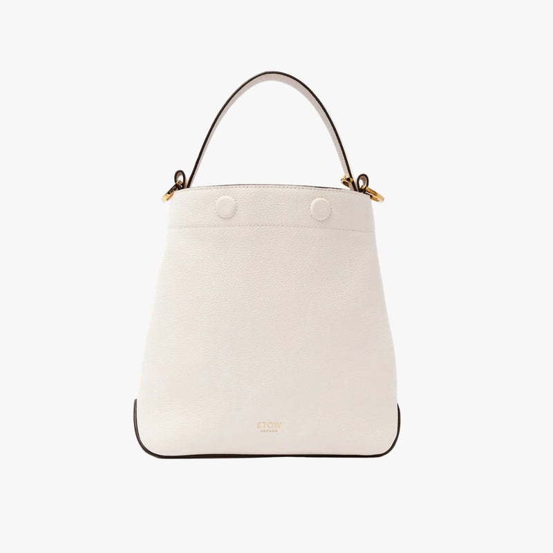 STOW London's Midi Curve in Spring Moon pebbled leather styled as a bucket bag featuring gold-coated stainless steel hardware on a light grey background