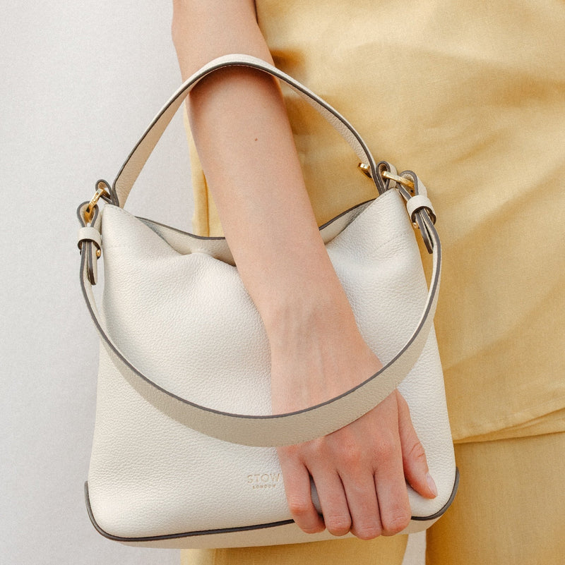 Model holding Model wearing STOW London's Midi Curve in Spring Moon leather featuring the detachable shoulder strap and top handle with gold hardware and details 