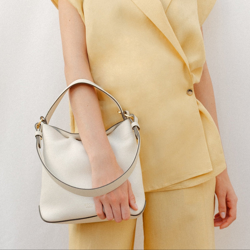 Model holding STOW London's Midi Curve in Spring Moon leather featuring the detachable shoulder strap with gold hardware and details 
