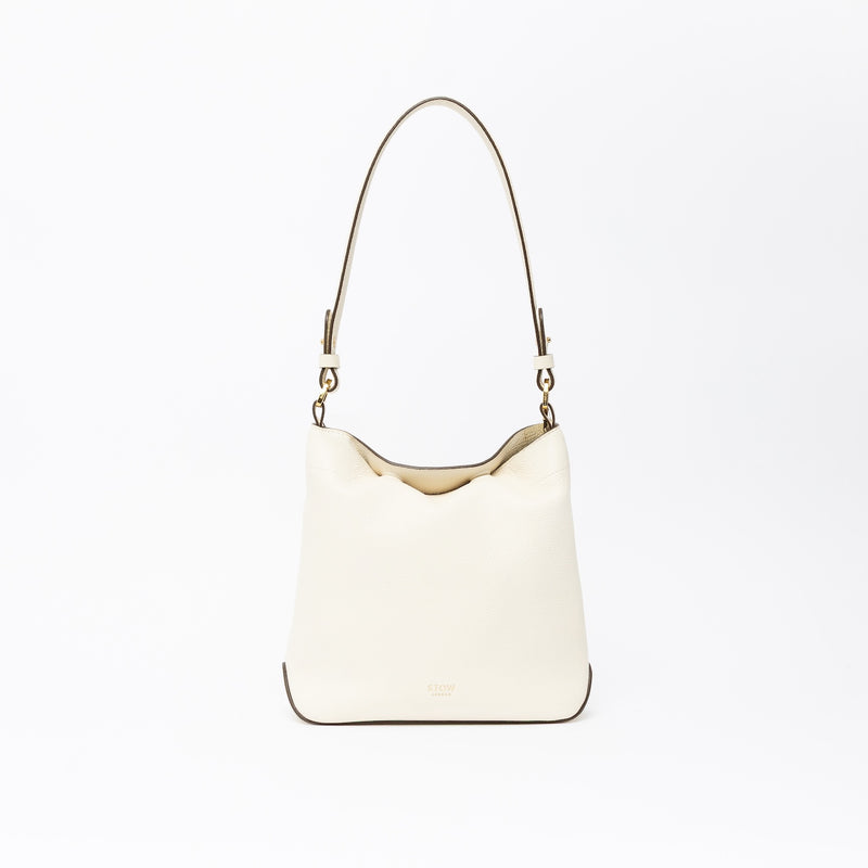 STOW London's Midi Curve in Spring Moon leather on a light grey background featuring the detachable shoulder strap with gold hardware and details 