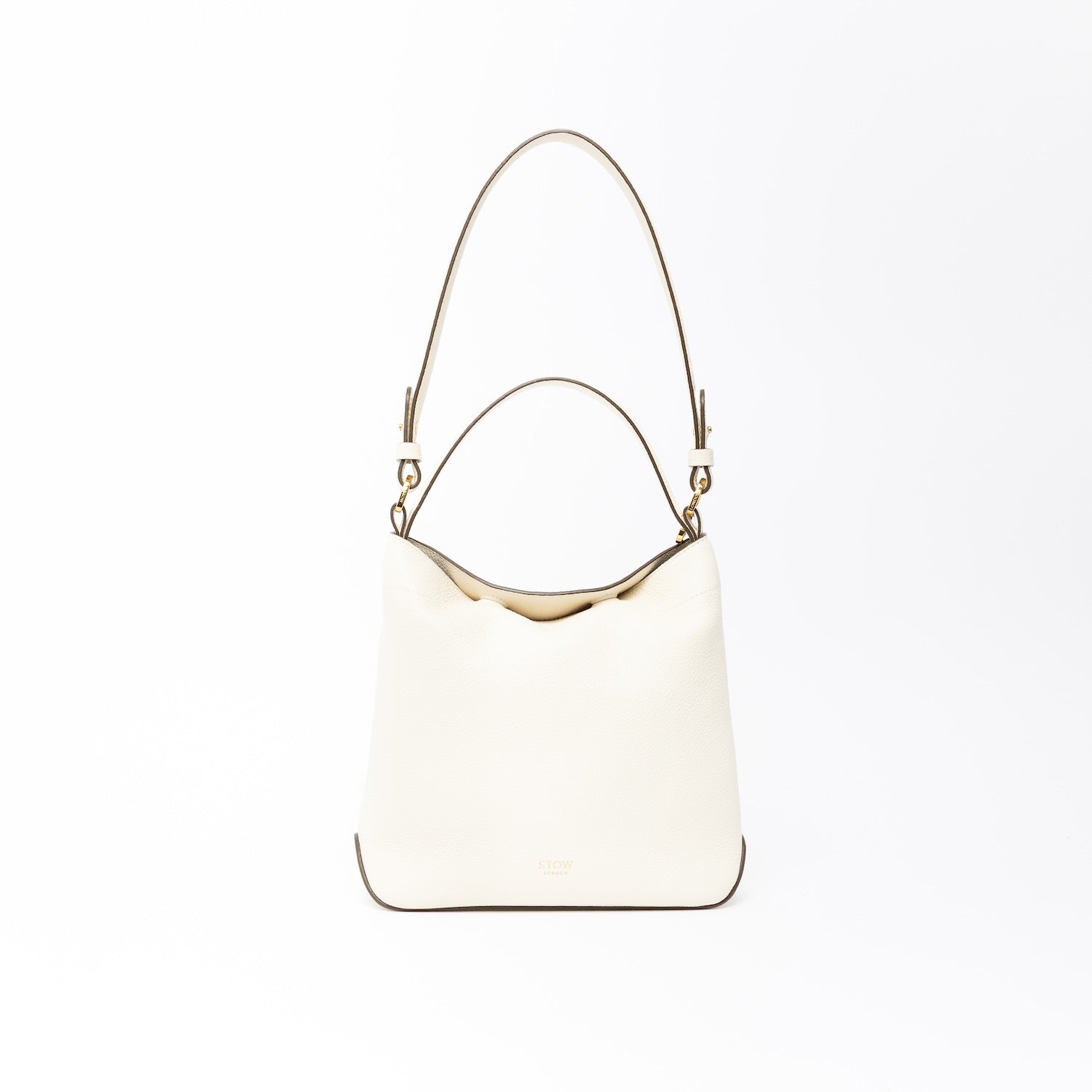 STOW London's Midi Curve in Spring Moon leather on a light grey background featuring the detachable shoulder strap and top handle with gold hardware and details 