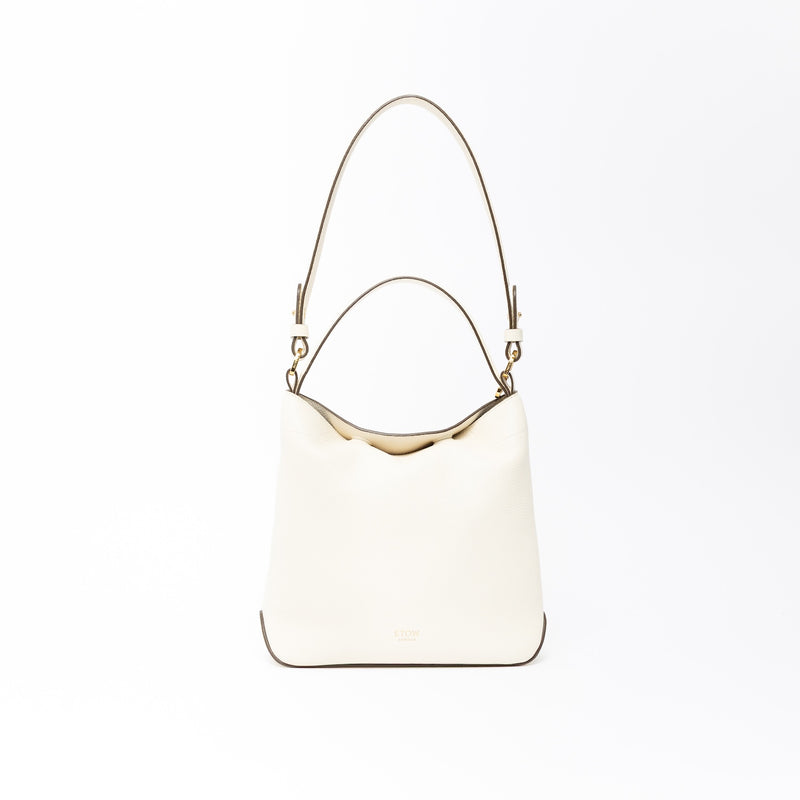 STOW London's Midi Curve in Spring Moon leather on a light grey background featuring the detachable shoulder strap and top handle with gold hardware and details 