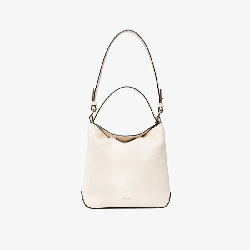 STOW London's Midi Curve in Spring Moon leather on a light grey background featuring the detachable shoulder strap with gold hardware and details 