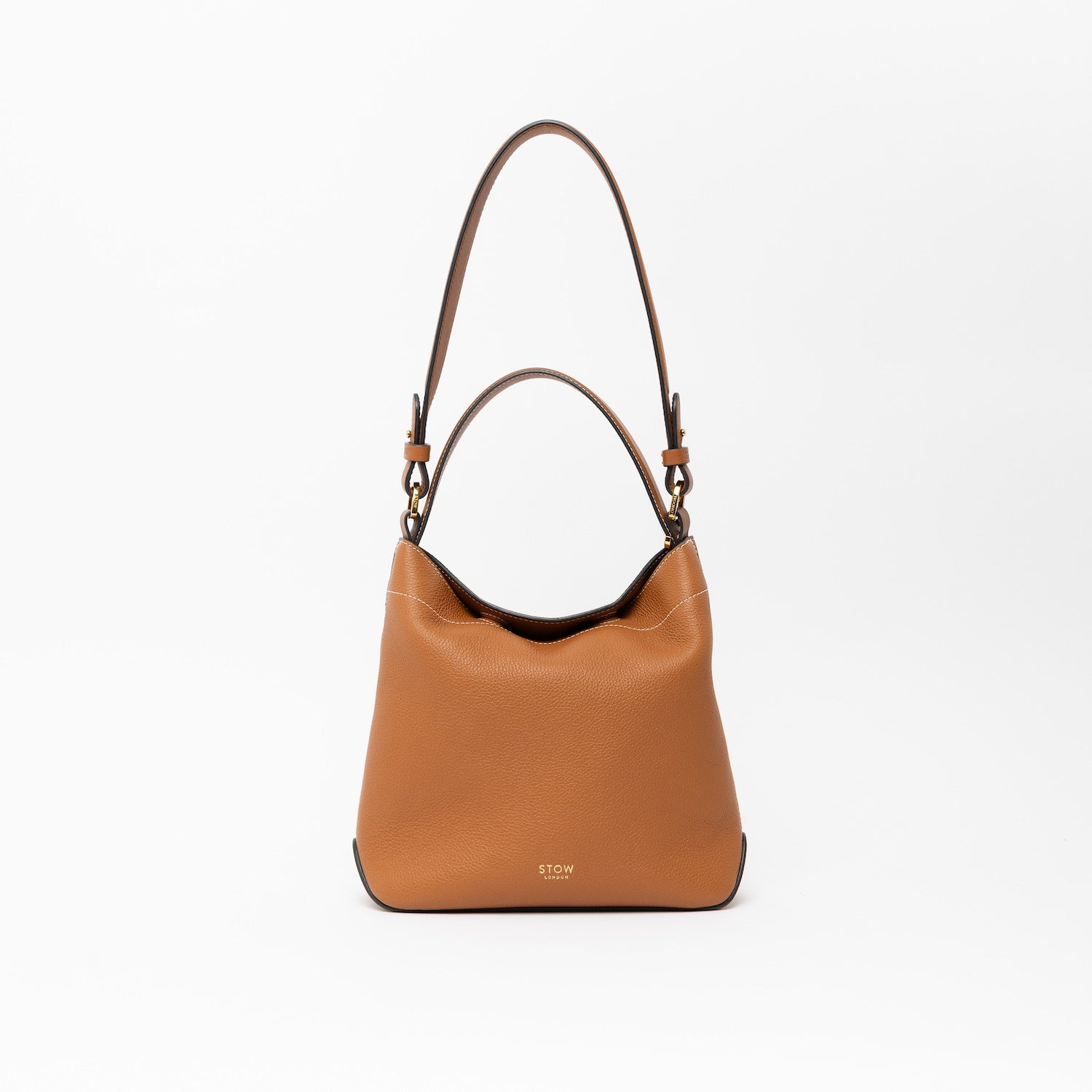 STOW London's Midi Curve in Earth Tan leather with the detachable shoulder strap with top handle out on a light grey background featuring gold details 
