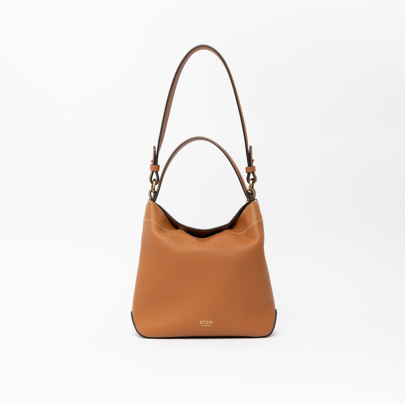 STOW London's Midi Curve in Earth Tan leather with the detachable shoulder strap with top handle out on a light grey background featuring gold details 