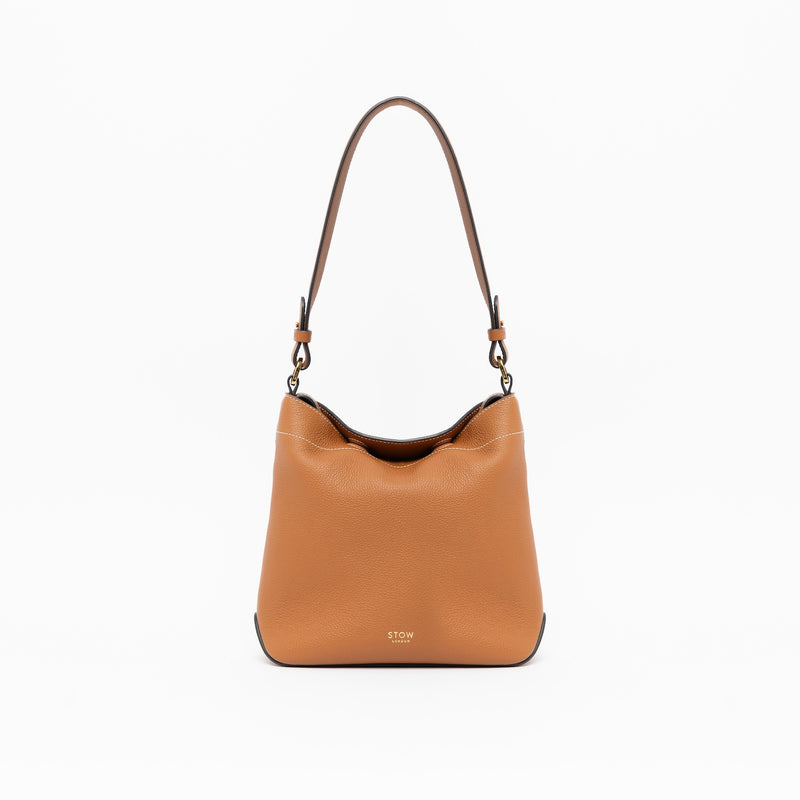 STOW London's Midi Curve in Earth Tan leather with the detachable shoulder strap on a light grey background featuring gold details 