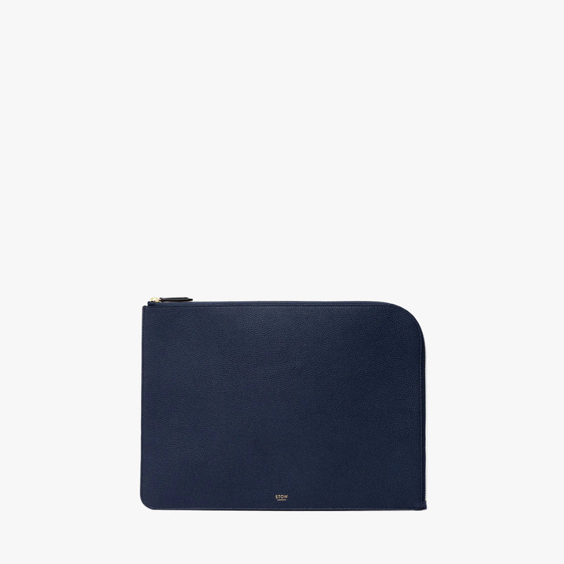 STOW London's Midi Leather Sleeve in Navy pebbled leather on a light grey background featuring a YKK Natulon Zip and a fine gold embossed logo on the front bottom. 