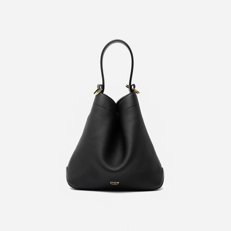 STOW London's Midi Curve in Black pebbled leather styled in a triangular shape featuring gold-coated stainless steel hardware on a light grey background